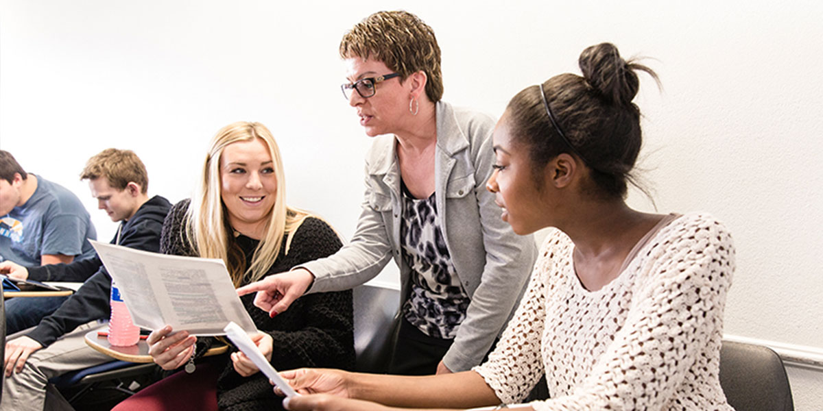 Professor helping two female students with an assignment in class